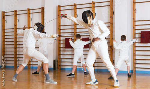 Portrait of children and adults fencers with trainer engaged in fencing in gym