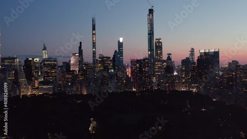 AERIAL: Wide view of Manhattan Skyline at night with flashing City lights and new skyscrapers in New York City at Central Park 