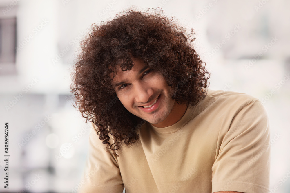 A MAN WITH CURLY HAIR HAPPILY SITTING AND LOOKING AT CAMERA A MAN WITH CURLY HAIR HAPPILY SITTING AND LOOKING AT CAMERA