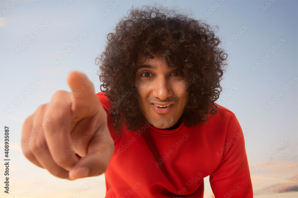 A YOUNG MAN WITH CURLY HAIR HAPPILY POINTING FINGER TOWARDS CAMERA A YOUNG MAN WITH CURLY HAIR HAPPILY POINTING FINGER TOWARDS CAMERA
