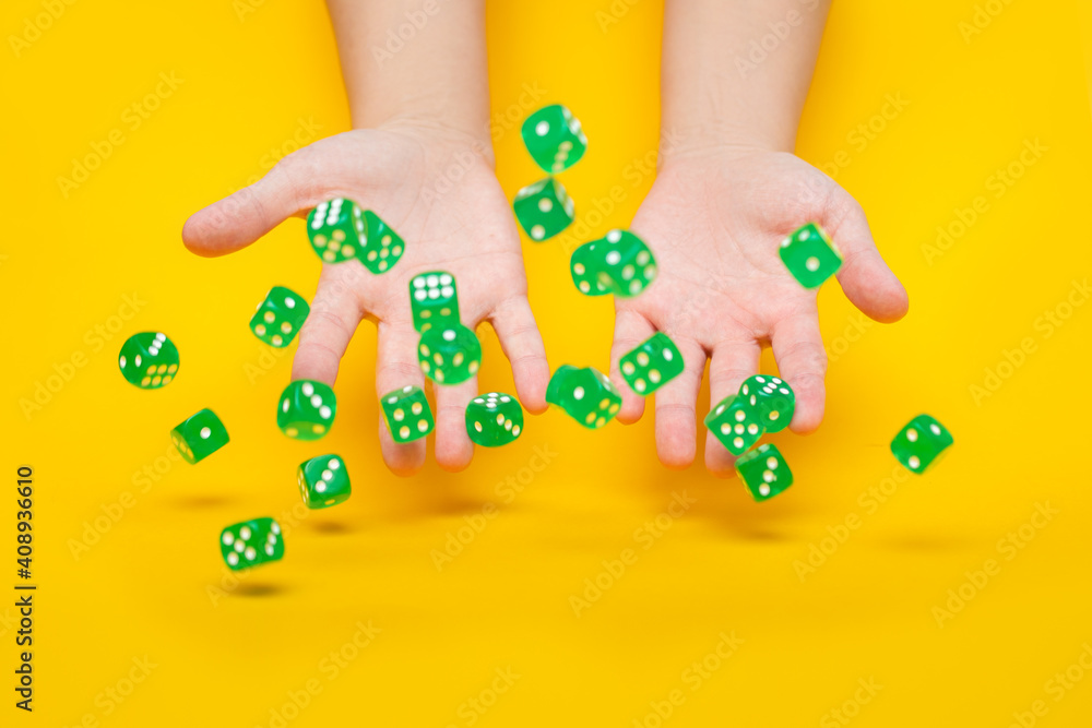 A lot of green dice fall from the hands on a yellow background: board games, selective focus on the hands, a photo in motion A lot of green dice fall from the hands on a yellow background: board games, selective focus on the hands, a photo in motion
