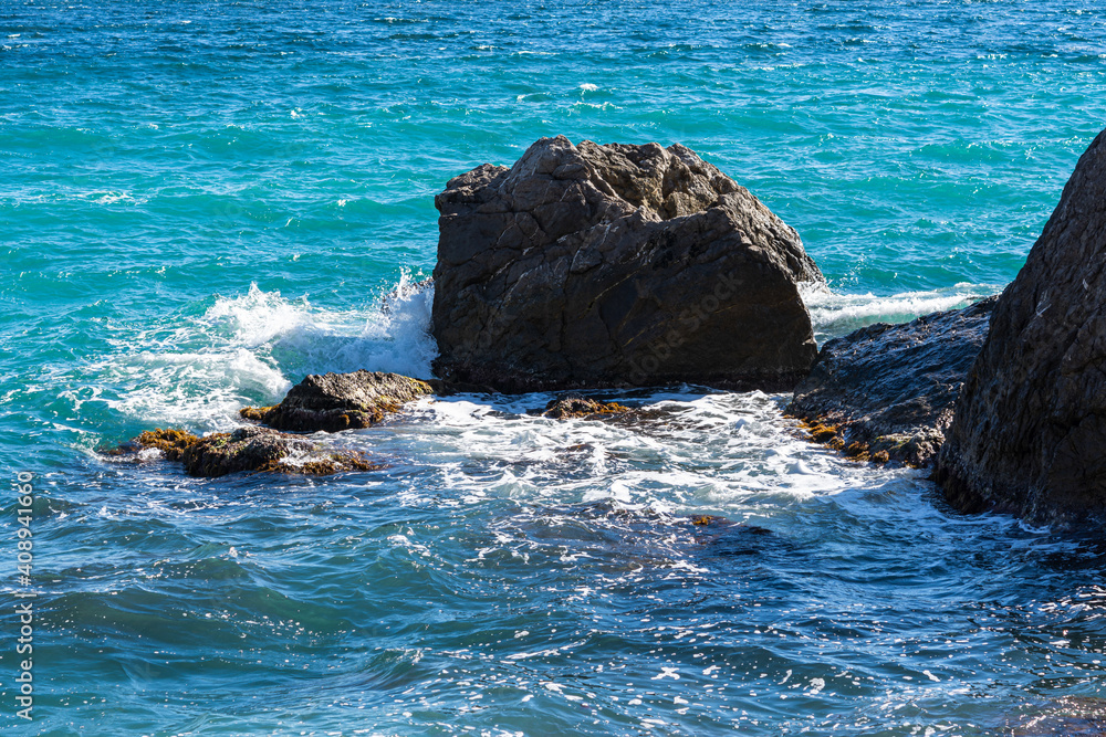 Turquoise sea stone beach, breaking waves in bright sunlight. Colorful bright sea background. The concept of summer, vacation, travel. The purest clear sea water, large stones on the beach close-up
