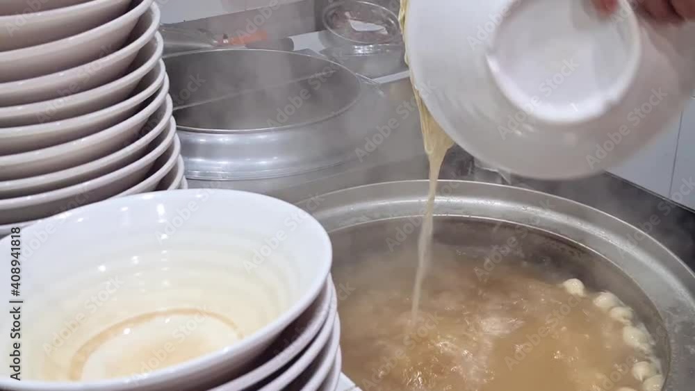 Noodles Cooked In Clear Soup Broth Picked Up By Chopsticks And Put Into Bowl - Close Up Noodles Cooked In Clear Soup Broth Picked Up By Chopsticks And Put Into Bowl - Close Up
