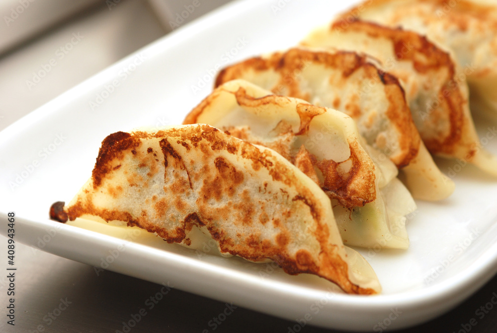 Japanese dumplings or Gyoza in white plate with gyoza sauce on a wooden table in a restaurant. Selective focus