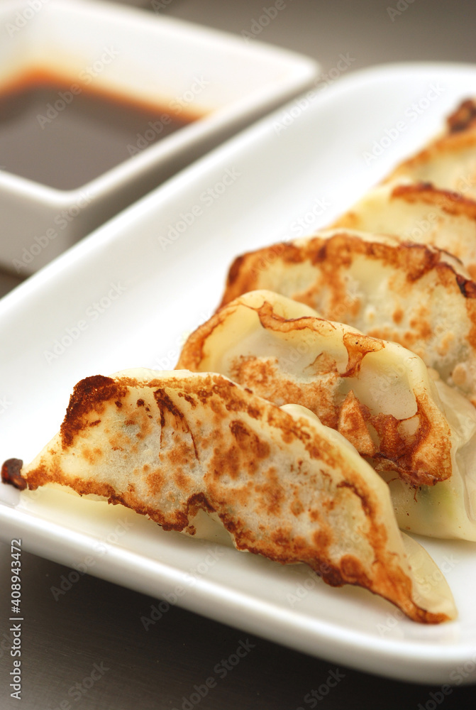 Japanese dumplings or Gyoza in white plate with gyoza sauce on a wooden table in a restaurant. Selective focus Japanese dumplings or Gyoza in white plate with gyoza sauce on a wooden table in a restaurant. Selective focus