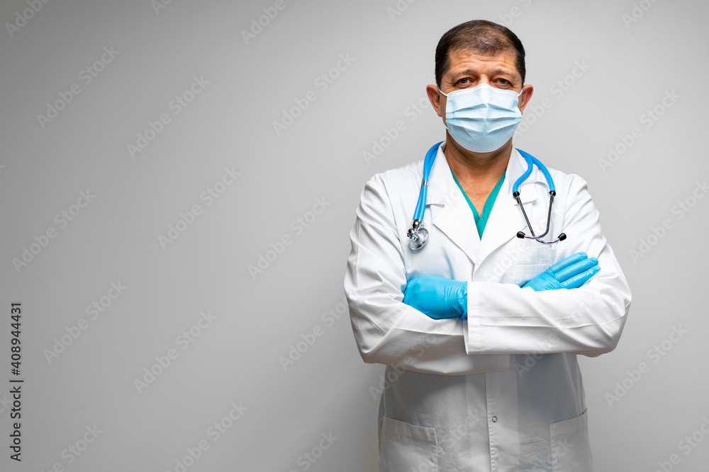 Senior male doctor in face mask standing against grey background Senior male doctor in face mask standing against grey background