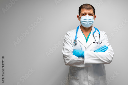 Senior male doctor in face mask standing against grey background