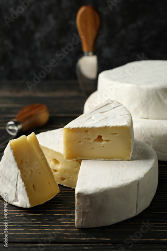 Camembert cheese and knives on wooden background, close up