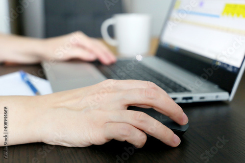 Female hands on laptop keyboard and computer mouse. Woman works with docs sitting at the desk