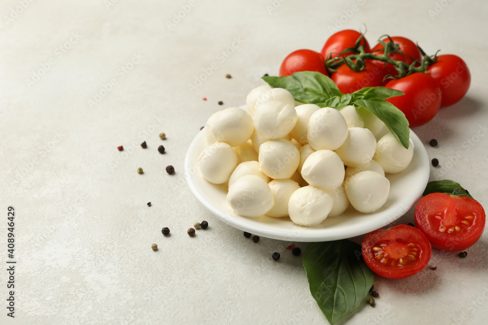 Plate with mozzarella and basil, tomato and pepper on white textured background, space for text