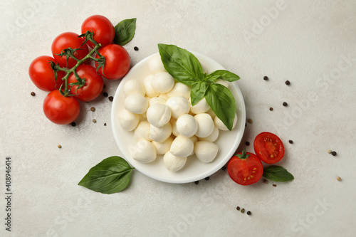 Plate with mozzarella and basil, tomato and pepper on white textured background, top view