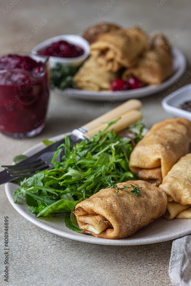 Homemade stuffed thin pancakes or crepes with meat, spicy cranberry sauce and arugula, light stone background. Traditional Russian cuisine for Maslenitsa. Shrove Tuesday.