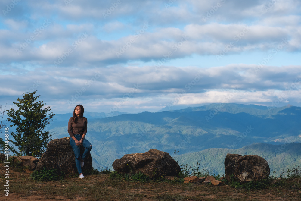 Portrait image of a young female traveler sitting on the rock with a beautiful cloudy sky and mountains view