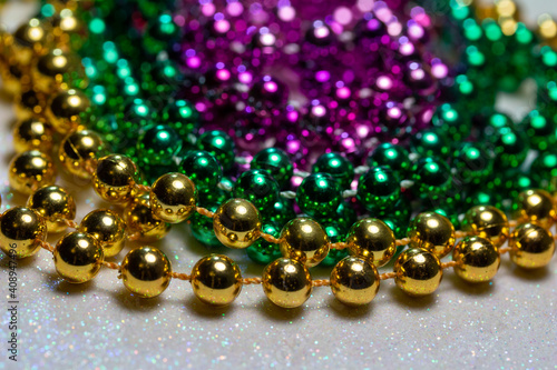 Macro defocused abstract view of traditional three-color Mardi Gras beaded costume jewelry necklaces on a sparkling white glitter texture background