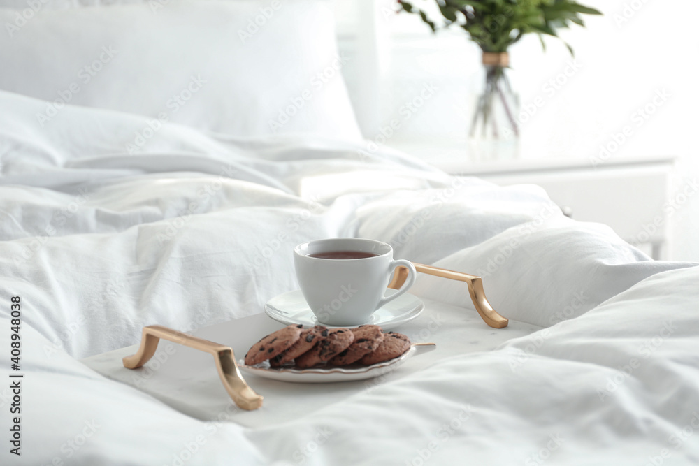 Cup of aromatic tea and cookies on soft blanket in bedroom