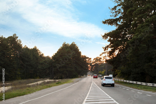 Highway near forest with cars at sunset. Road trip