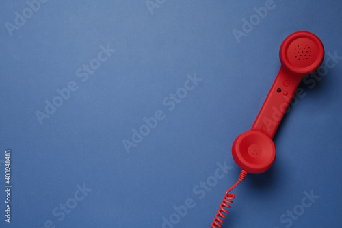 Fotografija Red corded telephone handset on blue background, top view