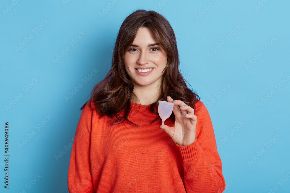 Close up portrait of European woman holding menstrual cup isolated over blue background, happy female, having period, dislike to use napkins or tampons, choosing alternative variant. Close up portrait of European woman holding menstrual cup isolated over blue background, happy female, having period, dislike to use napkins or tampons, choosing alternative variant.