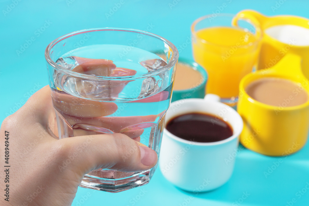 Female hand holds glass of water on background of other mugs with drinks. Female hand holds glass of water on background of other mugs with drinks.