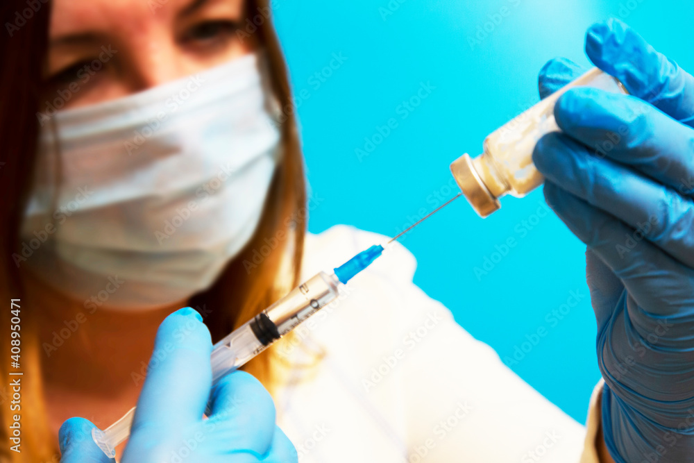Doctor filling syringe with medication, closeup. Vaccination and immunization. A female doctor wearing a mask and gloves with an ampoule and a syringe on a blue background Doctor filling syringe with medication, closeup. Vaccination and immunization. A female doctor wearing a mask and gloves with an ampoule and a syringe on a blue background