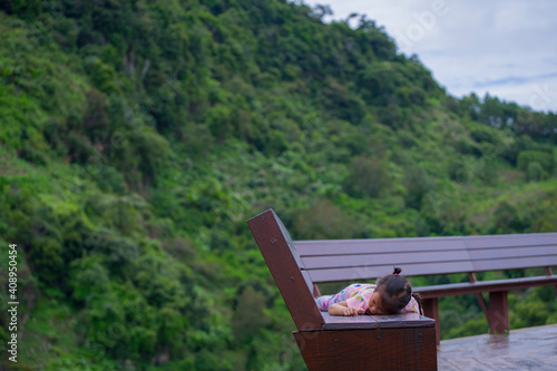 Sad little child girl lying down on brown wooden bench alone. photo