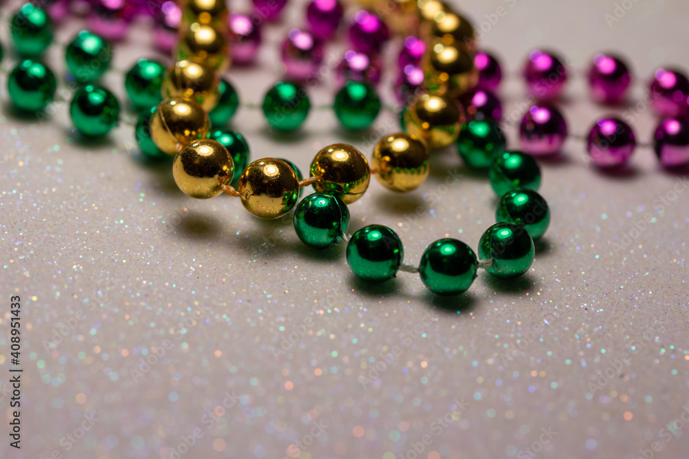 Macro defocused abstract view of traditional three-color Mardi Gras beaded costume jewelry necklaces on a sparkling white glitter texture background Macro defocused abstract view of traditional three-color Mardi Gras beaded costume jewelry necklaces on a sparkling white glitter texture background