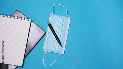 Flat lay tablet pc white notebook isolated blue background. Digital modern gadget, remote distance work concept. Face travel surgical hygienic disposable mask. Work at home concept.
