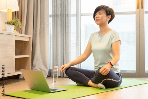 Home workout during Covid 19 pandemic lock down. A healthy asian woman in asana posture with eyes closed, she follow the step from online yoga programs in the website. Happy self isolation, New normal