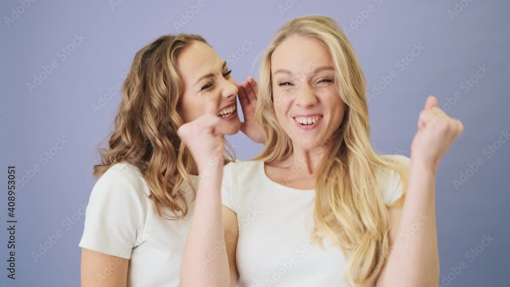 Close-up view of two positive women are sharing happy news standing isolated over white background in studio Close-up view of two positive women are sharing happy news standing isolated over white background in studio