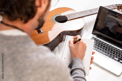 Man writing in a notebook while learning to play the guitar at home.