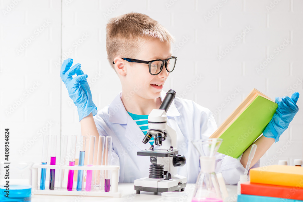 A schoolboy with a microscope and book examines chemicals in test tubes, conducts experiments - a portrait on a white background. Concept for the study of coronavirus in the laboratory A schoolboy with a microscope and book examines chemicals in test tubes, conducts experiments - a portrait on a white background. Concept for the study of coronavirus in the laboratory