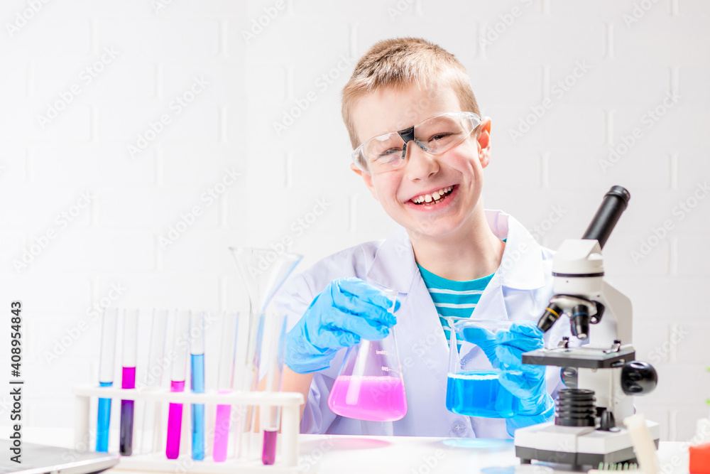 A schoolboy with a microscope examines chemicals in test tubes, conducts experiments - a portrait on a white background. Concept for the study of coronavirus in the laboratory A schoolboy with a microscope examines chemicals in test tubes, conducts experiments - a portrait on a white background. Concept for the study of coronavirus in the laboratory