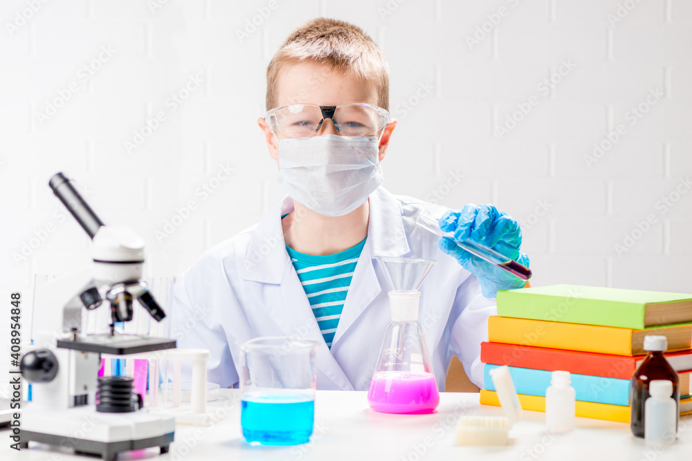 A schoolboy with a microscope and book examines chemicals in test tubes, conducts experiments - a portrait on a white background. Concept for the study of coronavirus in the laboratory A schoolboy with a microscope and book examines chemicals in test tubes, conducts experiments - a portrait on a white background. Concept for the study of coronavirus in the laboratory