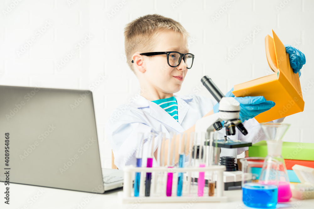 A schoolboy with a microscope and book examines chemicals in test tubes, conducts experiments - a portrait on a white background. Concept for the study of coronavirus in the laboratory A schoolboy with a microscope and book examines chemicals in test tubes, conducts experiments - a portrait on a white background. Concept for the study of coronavirus in the laboratory