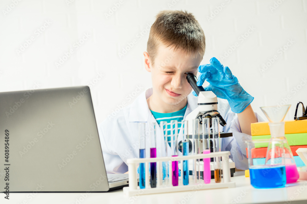 Schoolboy with a laptop in the laboratory conducts chemical experiments with substances in test tubes, portrait of a young chemist Schoolboy with a laptop in the laboratory conducts chemical experiments with substances in test tubes, portrait of a young chemist