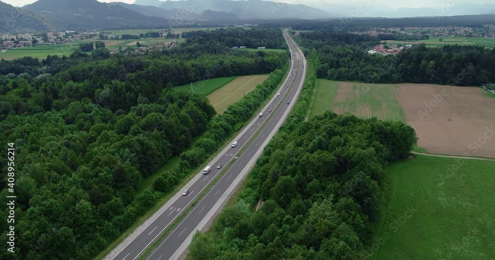 Elevated view of traffic on highway in Slovenia. High flying drone over motorway, forest and green farming fields. Alps mountains in the distance. Tilt up Elevated view of traffic on highway in Slovenia. High flying drone over motorway, forest and green farming fields. Alps mountains in the distance. Tilt up