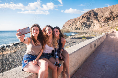 Fotografie Group of three woman in friendship taking selfies and using phone near the beach