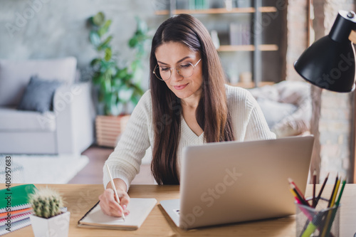 Photo of beautiful attractive happy positive smiling focused calm woman writing in notebook working in laptop at home house