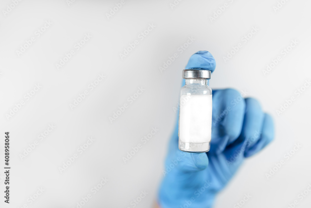 Healthcare cure concept with a hand in blue medical gloves holding Coronavirus, Covid 19 virus, vaccine vial in glass bottle on white background. Copy space, close up. Healthcare cure concept with a hand in blue medical gloves holding Coronavirus, Covid 19 virus, vaccine vial in glass bottle on white background. Copy space, close up.
