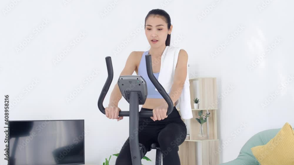 Beautiful asian woman riding on exercise bike at home. Beautiful asian woman riding on exercise bike at home.