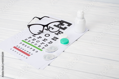 Flat composition with contact lenses, table for eye examination. Accessories for ophthalmologists. Glasses and lenses for vision correction on a blue background