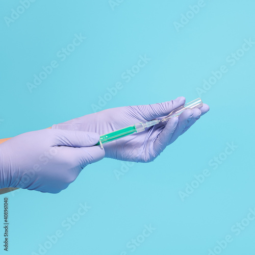 Syringe for injection in hand, latex medical gloves on hand. On a blue background.