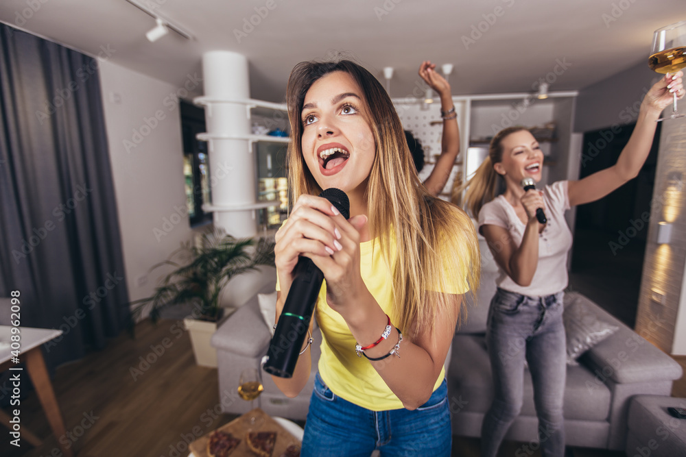 Group of young women spend free time in karaoke, sing and have fun together, with friends, at home.