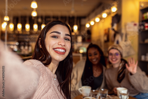 Three young multi ethnic women enjoy coffee at a coffee shop and making selfie.