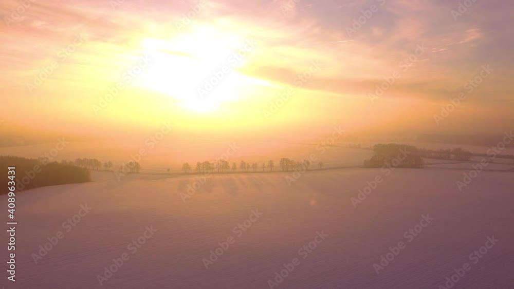 Aerial fairy-tale view of the wintery countryside. Snow-covered fields, trees casting long shadows, rising sun shining straight in the camera. Aerial fairy-tale view of the wintery countryside. Snow-covered fields, trees casting long shadows, rising sun shining straight in the camera.