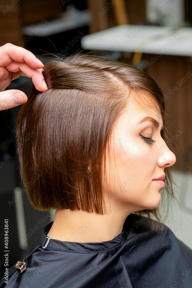 Fototapeta premium A male hairdresser is straightening the hair of the young woman in a beauty salon
