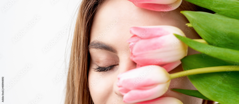 Half face portrait of a happy young caucasian woman with closed eyes and pink tulips cover her face against a white background Half face portrait of a happy young caucasian woman with closed eyes and pink tulips cover her face against a white background