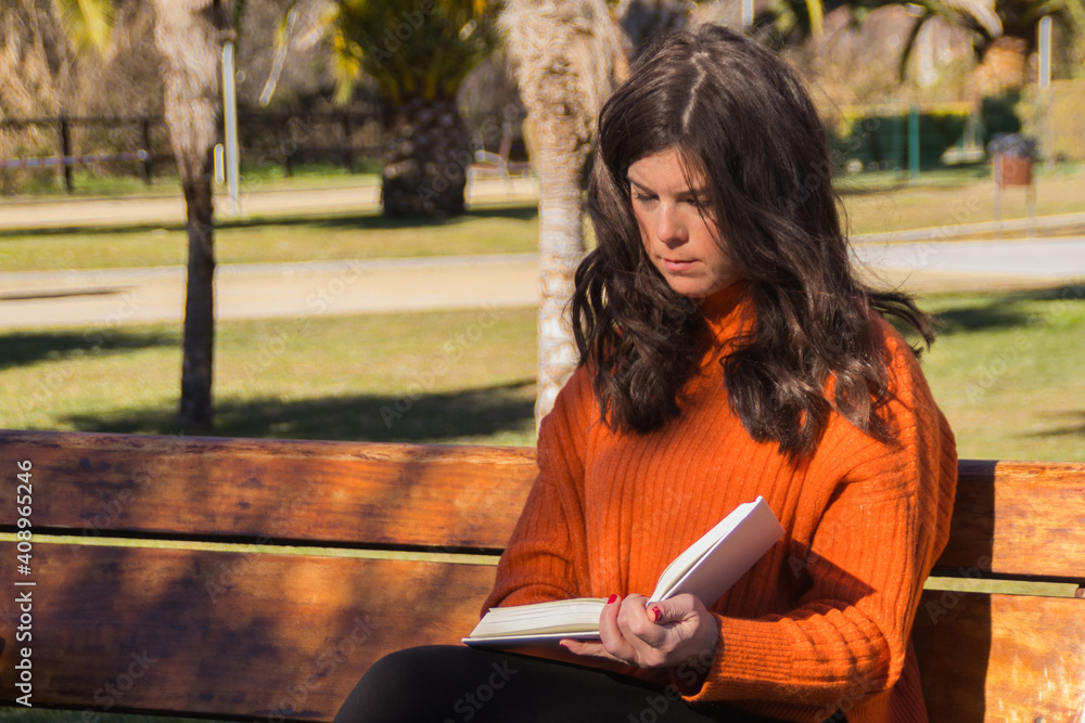 Woman reading a book sitting on a bench in a park on a sunny day. Woman reading a book sitting on a bench in a park on a sunny day.