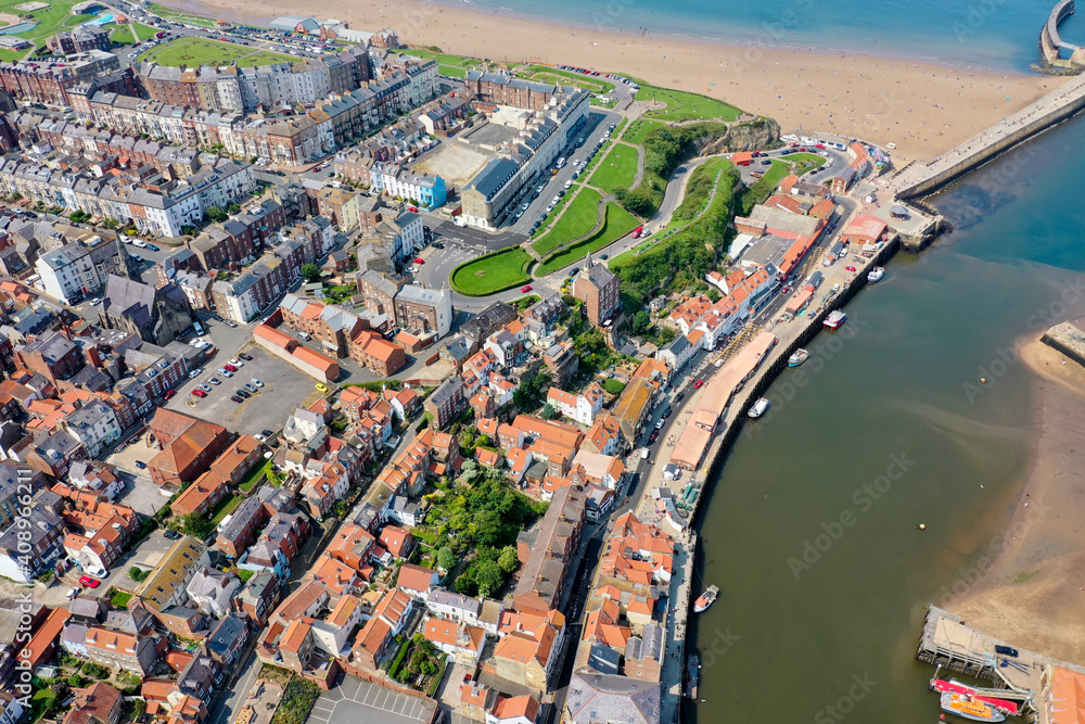 Aerial photo of the beautiful town of Whitby in the UK, North Yorkshire in the UK showing a top down view of the village by the harbour and sandy beach on a hot sunny summers day