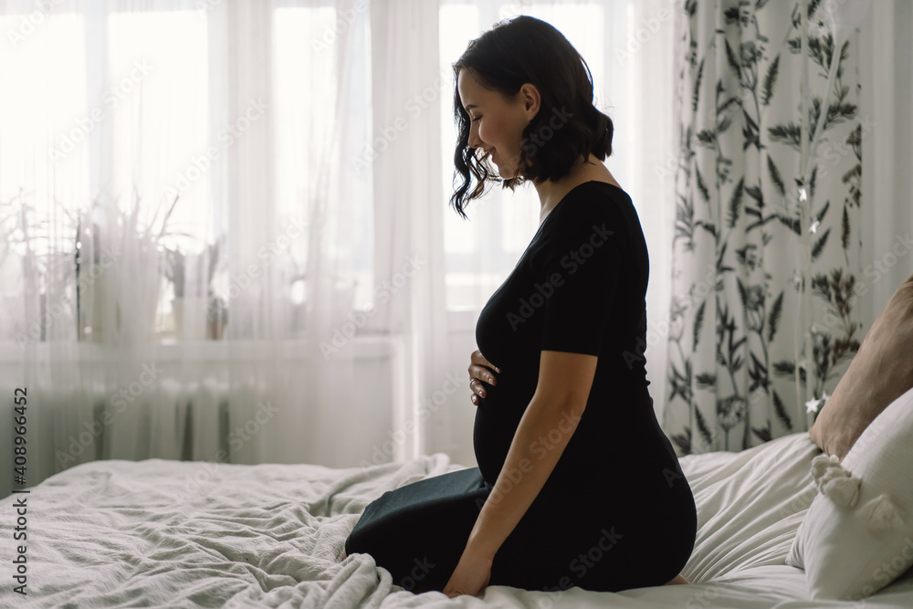 Attractive pregnant woman is sitting in bed and holding her belly. Pregnancy Concept.